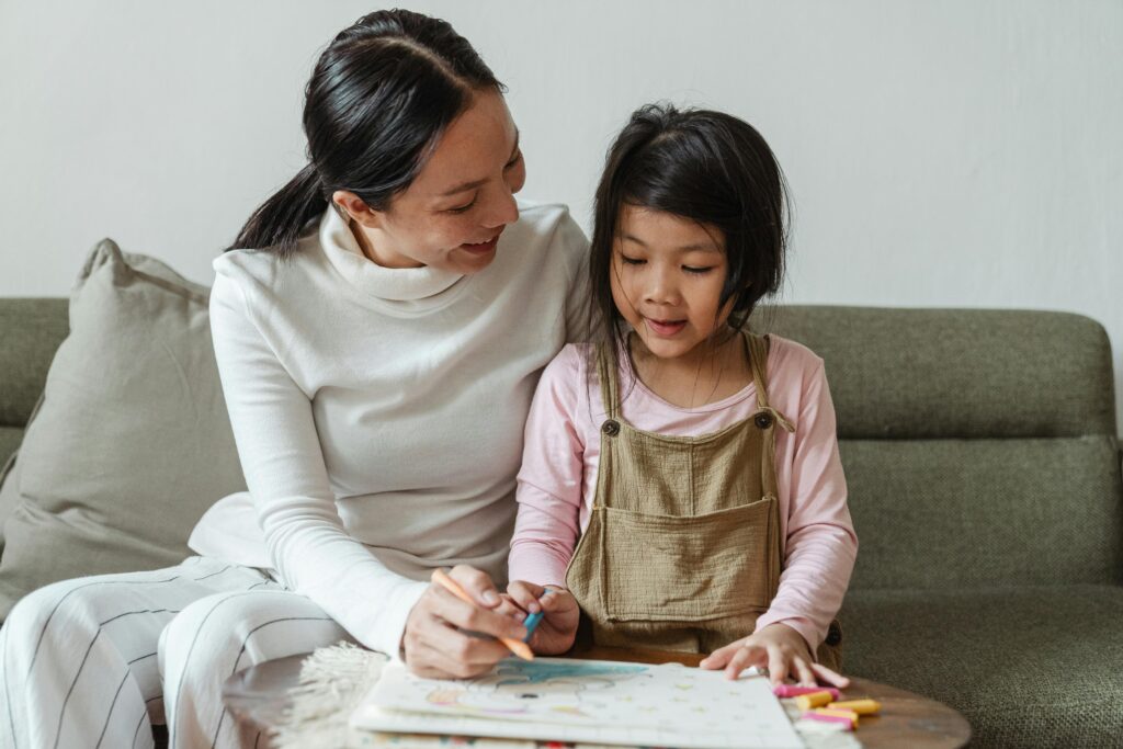 pexels-photo-4474005-4474005 A mother helps her young daughter with a colorful drawing at home, fostering creativity and bonding.